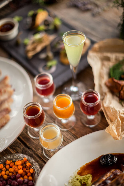 Shots cherry lemon apple cranberry on wooden table at feast with plates daylight restaurant  - Zdjęcie, obraz