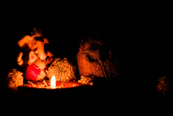 extreme low light photography of ganpati statue with shining diya and dry coconut on black background. religious concept - Photo, Image