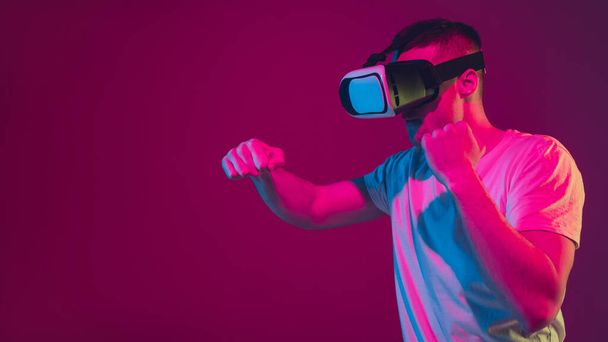 Caucasian mans portrait isolated on pink-purple studio background in neon light, playing with VR-headset - Foto, immagini