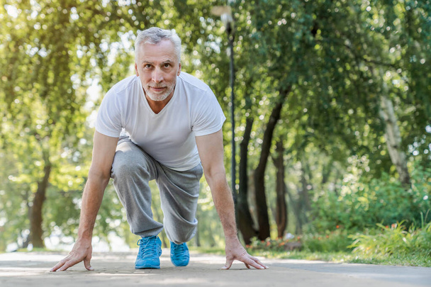 Healthy lifestyle concept. Cheerful senior man starting to jogging in park - Foto, Imagem