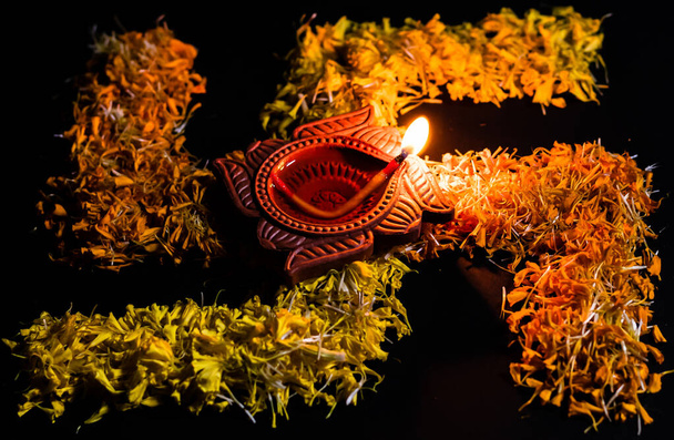 esvástica hecha con pétalos de flores y lámpara de arcilla que brilla sobre ella sobre fondo negro. concepto de fe y creencia
 - Foto, imagen
