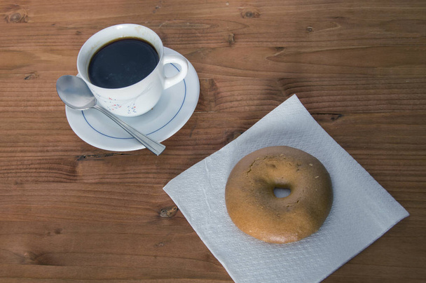 чашку кофе с бубликом на салфетке, изолированной на деревянном фоне
 - Фото, изображение