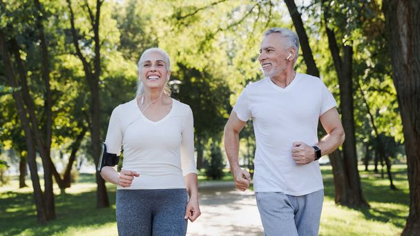 Elderly man and old woman in headphones jogging together outside - Photo, image