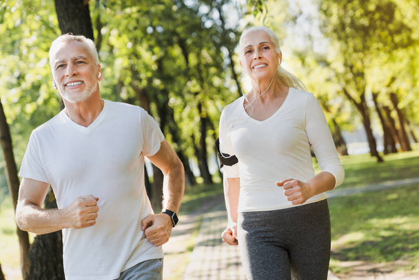 Portrait of elderly man and old woman in headphones jogging toge - Photo, image