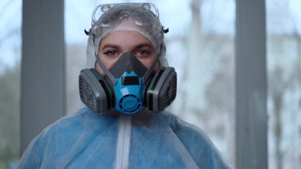 Portret van een vrouwelijke arts die beschermende kleding weert tijdens een coronavirus pandemie. Vrouwelijke arts in gevarenpak, ademhalingsmasker, handschoenen en bril die zich klaarmaken voor de werkdag in kliniek of ziekenhuis - Video