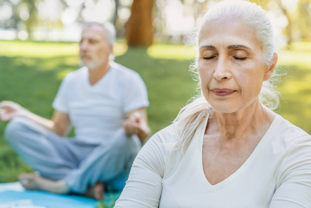 Yoga at park. Close up shot of senior couple sitting in lotus pose on green grass in calm and meditation - Foto, immagini
