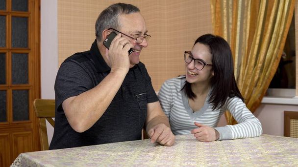 La hija le enseña a papá a usar el teléfono. Una joven le muestra a su padre dónde hacer clic en un teléfono inteligente. El hombre llamó por teléfono. La familia está sentada en una habitación cómoda
. - Foto, imagen