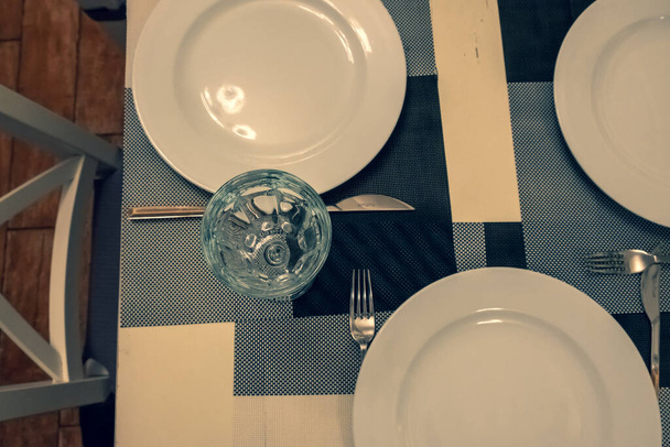  A mesa servida no restaurante. Limpar pratos e eletrodomésticos na toalha de mesa em um café. Óculos transparentes brilhantes. Placas brancas. Preparado para a recepção dos hóspedes. Serviço de alta
. - Foto, Imagem