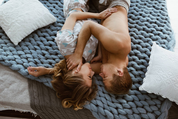 Couple in the bedroom on the bed in the bedroom. A blonde girl in pajamas, a guy with a naked torso. Love and hugs. A beautiful couple. New Year's interior. Christmas time. A blanket of large mating. - Photo, image
