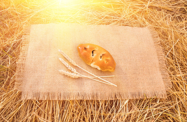 Un bollo fresco acostado sobre un mantel con espiga de trigo, primer plano
 - Foto, Imagen