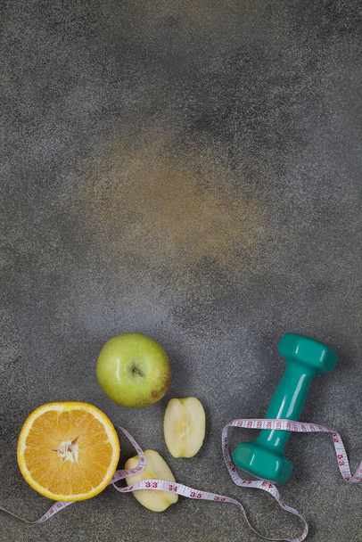 πράσινο dumbbell με μέτρηση, μήλο και πορτοκάλι σε σκούρο φόντο. αντιγραφή χώρου κοντά. υγιεινό τρόπο ζωής έννοια επίπεδη θέσει επάνω όψη κάθετη - Φωτογραφία, εικόνα