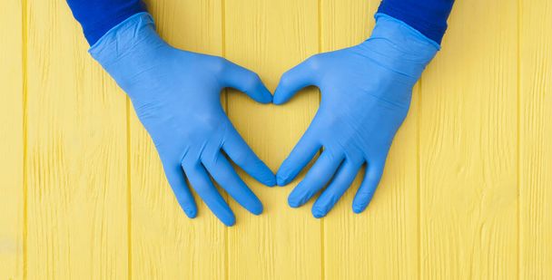 Guantes azules de nitrilo. Manos de un médico en los guantes de látex azul sobre una pancarta de madera amarilla
 - Foto, Imagen