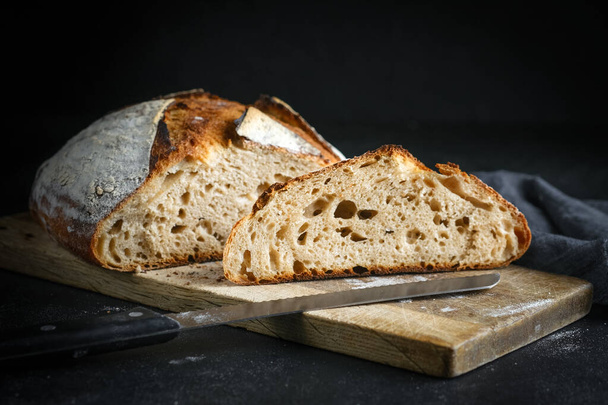 パンだ。暗めの背景のコピースペースにナイフでまな板に自家製の全粒穀物パンをスライス. - 写真・画像