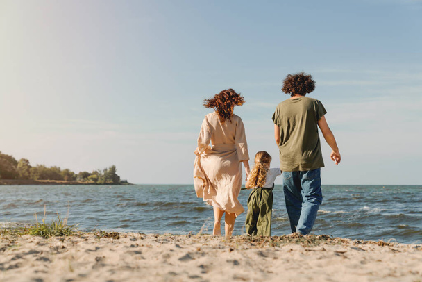 Rear view of happy family walking and having fun on the beach with cute little girl - Fotoğraf, Görsel
