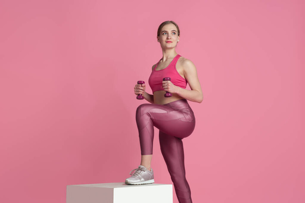 Beautiful young female athlete practicing on pink studio background, monochrome portrait - Photo, image
