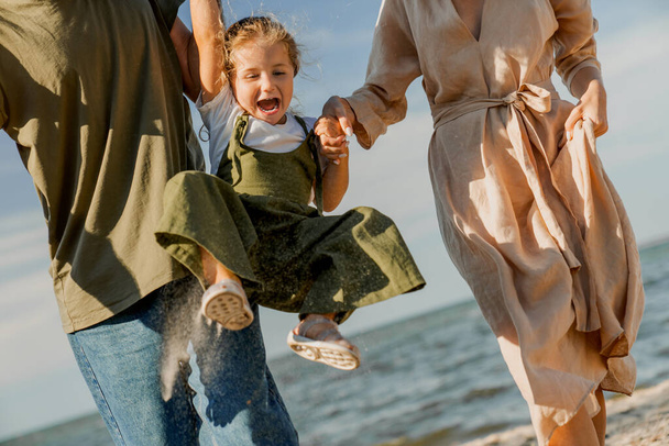 Plan recadré d'une famille heureuse marchant et s'amusant sur la plage avec une fille mignonne heureuse
 - Photo, image