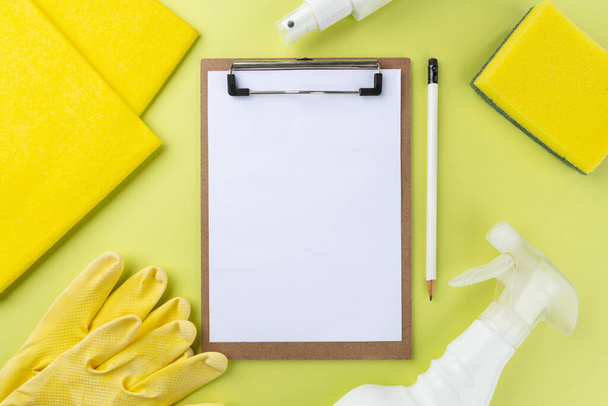 Various cleaning items on green background and blank notepad. Cleaning products concept. - Photo, Image