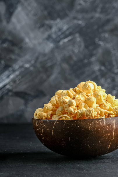 Kitschiges Popcorn in einer Kokosnussschale auf dunklem Hintergrund. - Foto, Bild