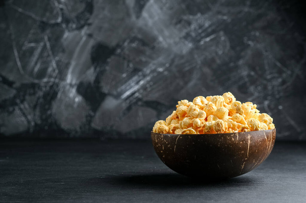 Kaas popcorn in een kokosnoot kom op een donkere achtergrond kopieer ruimte. - Foto, afbeelding