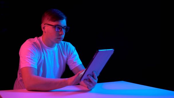 Young man with a tablet. A man is using a tablet. Blue and red light falls on a man on a black background. - Fotó, kép