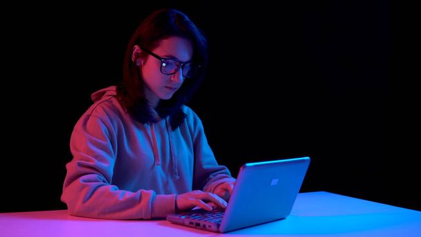 Young woman with a laptop. A woman is using a laptop. Blue and red light falls on a woman on a black background. - 写真・画像