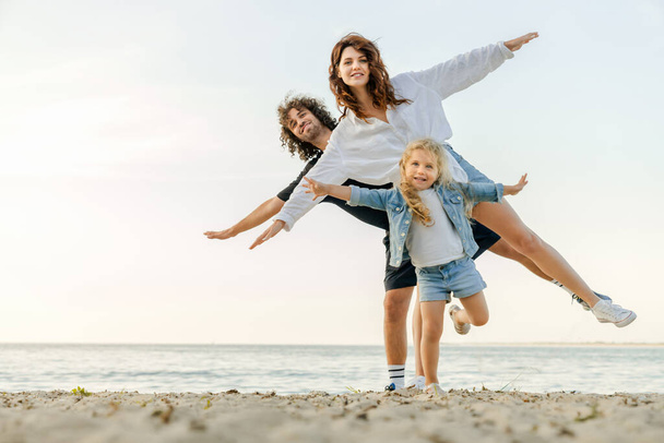 Young happy family having fun while doing yoga excercises on sunny beach - Φωτογραφία, εικόνα