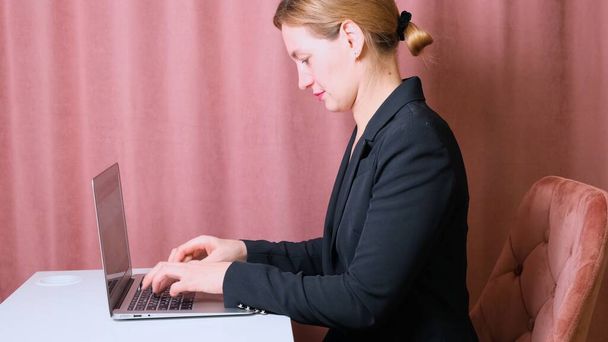 Komoly női titkár gépel egy laptopon, aki egy asztalnál ül a munkahelyén.. - Fotó, kép