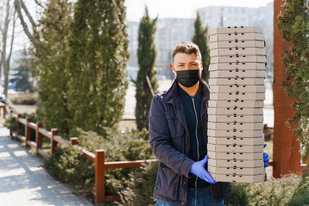 Lebensmittelkurier in medizinischen Handschuhen gibt 4 Kisten mit Pizza an Kunden, die zu Hause bleiben, weil das Coronavirus 19 Menschen tötet. Essen aus dem Restaurant mitnehmen - Foto, Bild