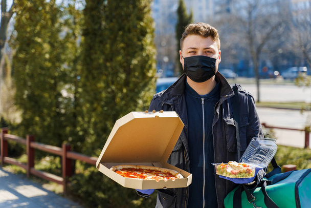 Sécurité livraison de nourriture du restaurant pendant la période de quarantaine. Courrier en masque médical avec pizza et salade en coffret. Sauvez votre vie du coronavirus covid 19
 - Photo, image
