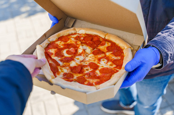 Müşteri karton kutudan bir dilim pizza alır. Coronavirus covid 19 'u durdurmak için tıbbi eldiven içinde yiyecek teslimatı.. - Fotoğraf, Görsel