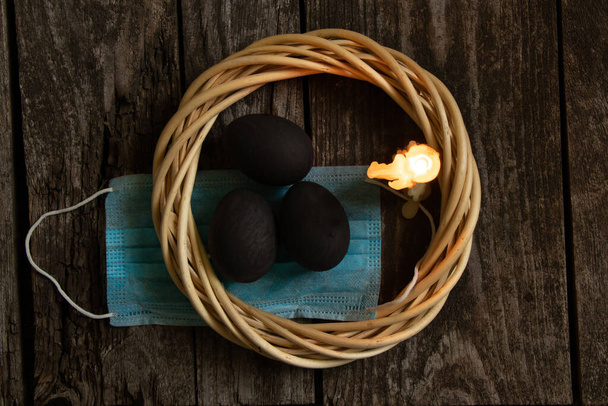 máscara médica e velas coloridas de chama de ovo preto no dia de Páscoa em uma mesa de madeira velha durante a pandemia
 - Foto, Imagem