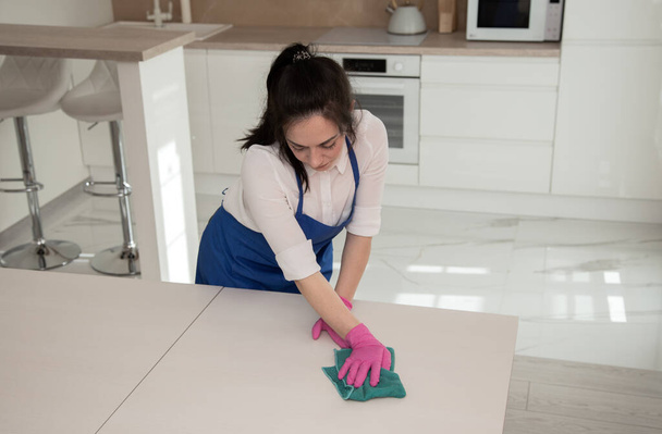 La fille fait un nettoyage complet dans la cuisine. Il essuie une surface blanche avec un chiffon en microfibre
. - Photo, image