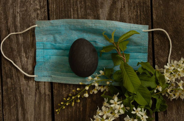 Tıbbi maske ve siyah yumurta Paskalya gününde salgın sırasında eski ahşap bir masada. - Fotoğraf, Görsel