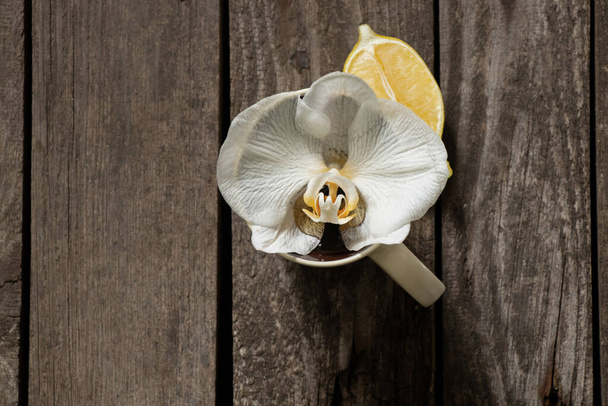 Phalaenopsis flower in cups and cut lemon with tea coasters on an board - Фото, изображение