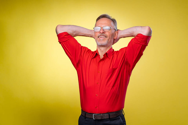 Aged, senior man is standing with hands over head. Relaxed. Isolated against yellow background - 写真・画像