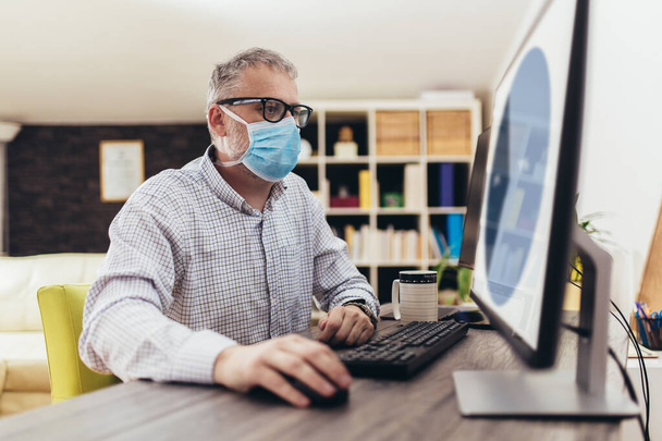 Homem de negócios a trabalhar em casa, usa uma máscara protectora. Quarentena devido a pandemia de coronavírus. Fique em casa
. - Foto, Imagem