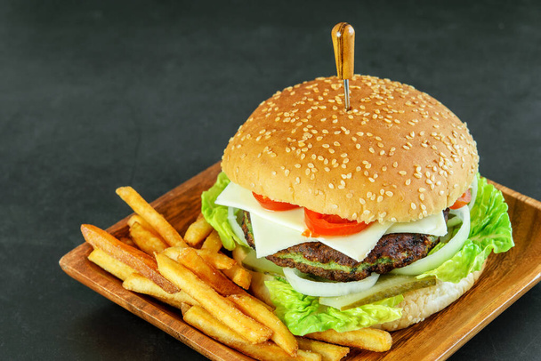 Vegetarische hamburger met spinazie en groente, aardappelfrietjes op de houten eco plaat, op de donkere achtergrond. Bovenaanzicht. Heerlijk fastfood voor vegetariërs.  - Foto, afbeelding