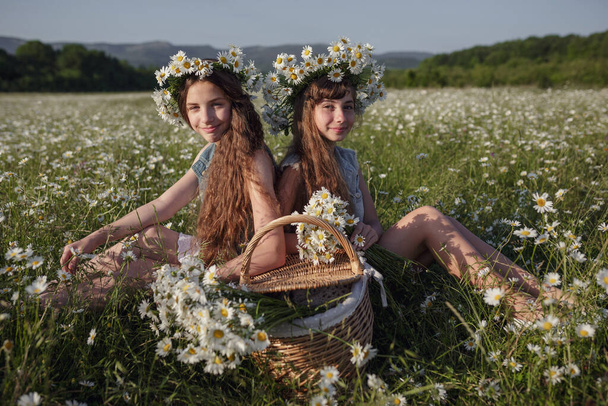 two cute teen girls in denim with beautiful healthy long brown hair in a daisy field. idea and concept of health, happy childhood, friendship - Foto, Imagen