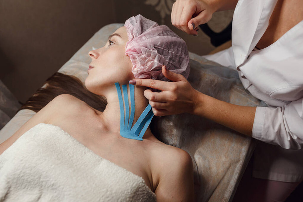Kobieta kosmetyczka nagrywająca twarz pacjenta leżącego na biurku w domu. Fizjoterapia i zabiegi kosmetologiczne. Metoda niechirurgicznego odmłodzenia skóry. Leczenie skóry twarzy. - Zdjęcie, obraz