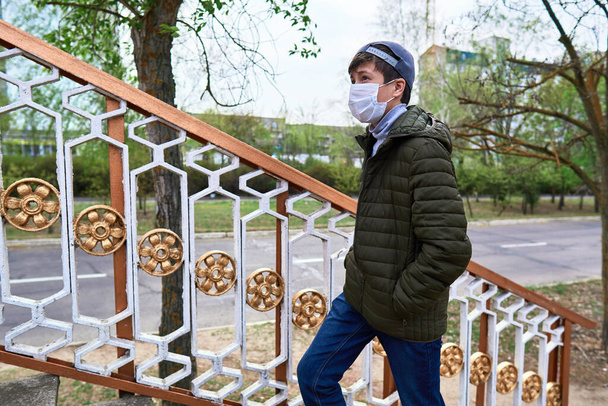 dospívající chlapec kráčí po ulici během dne, chodník a výškových budov s byty, obytná čtvrť, lékařská maska na tváři chrání před viry a prachem - Fotografie, Obrázek