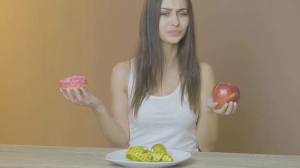 Woman with slender figure holding a donut and an apple - Metraje, vídeo