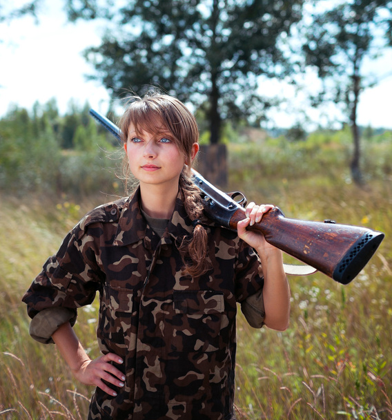 Young beautiful girl with a shotgun looks into the distance - Photo, Image