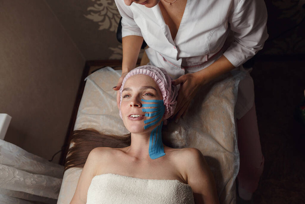 Face aesthetic taping. Facial skin care. Young woman lying with tape applications on face. Non-invasive anti-ageing lifting method for reduction of wrinkles on the forehead and the outer eye corners - Photo, Image