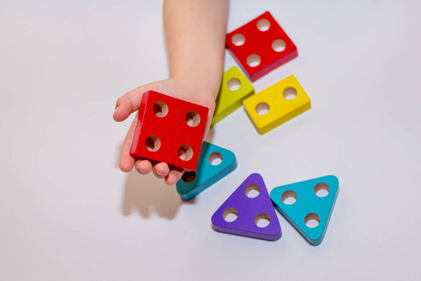Children's toy made of wood on a white background close-up, the child plays with the designer, sorter. Children's room with toys. Constructor in the hands of a child. Wooden houses in the background . Quarantined home schooling. - Photo, Image