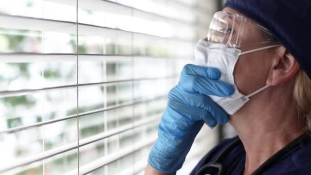 Stressed Doctor or Nurse On Break At Window Wearing Face Mask and Protective Glasses. - Video