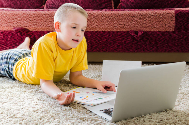 Дистанційне навчання онлайн-освіти. Школяр навчається вдома з ноутбуком. Хлопчик спілкується онлайн з учителем, лежачи на підлозі
. - Фото, зображення