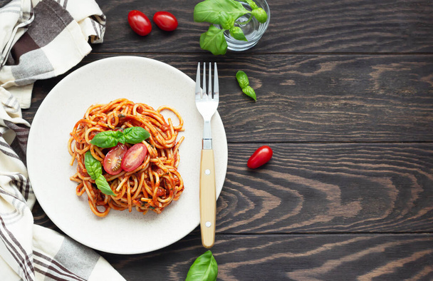 Tasty appetizing classic italian spaghetti pasta with tomato sauce, fresh cherry tomatoes and basil on ceramic plate. Wooden background, rustic style. Top view. - Foto, Bild