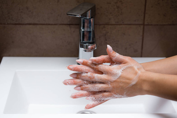 Κορίτσι πλένεται στα χέρια νεροχύτη με αντιβακτηριακό σαπούνι για την προστασία από την απειλή της μόλυνσης από τον ιό του στομίου κατά τη διάρκεια της αυτο-απομόνωσης - Φωτογραφία, εικόνα
