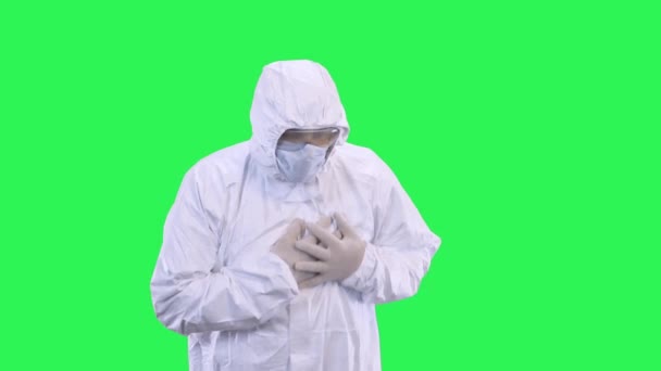 A man in a protective suit with a mask on his head and glasses holds on to a heart on a green background - Video