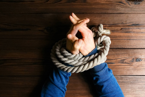Hands tied with a rope life-threatening on a wooden background. Slavery in business is human abuse. - Zdjęcie, obraz